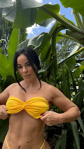 Mom in her 40s still showing off - A fun and catchy title for a video featuring a woman in her 40s wearing a yellow bikini and posing in a jungle setting.'